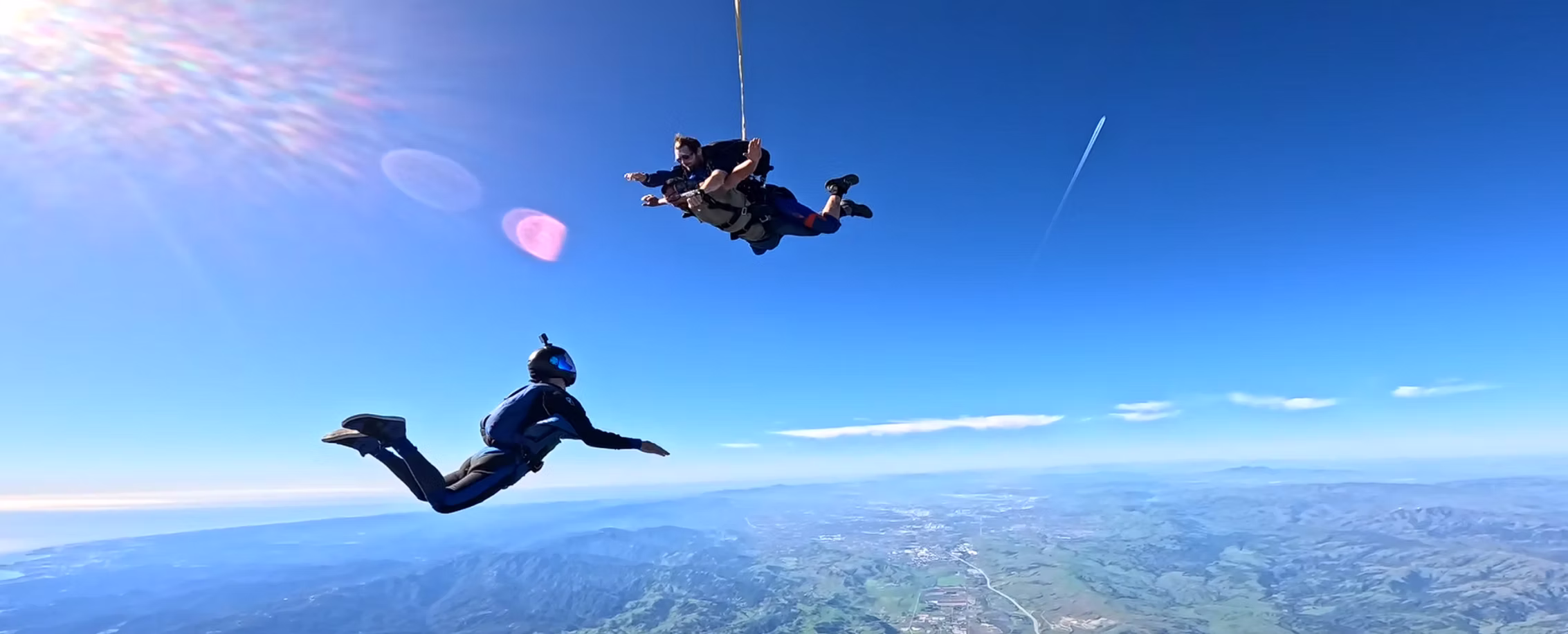 A tandem pair and a solo flyer sharing the sky over the coastline.