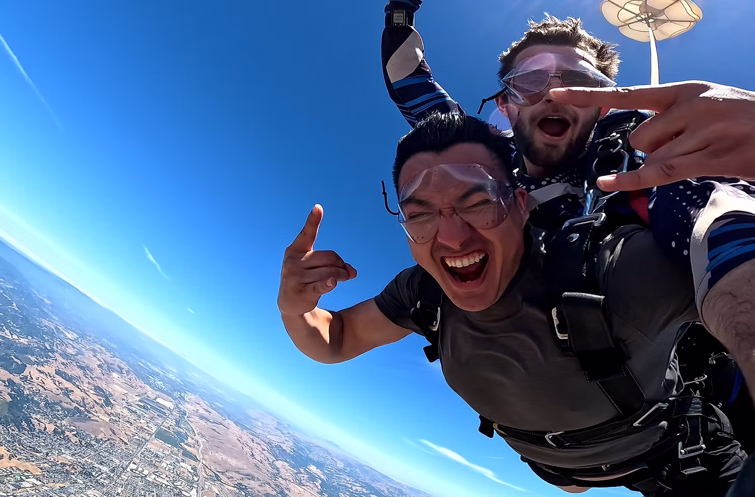 Two jumpers yelling with joy in freefall above the valley.
